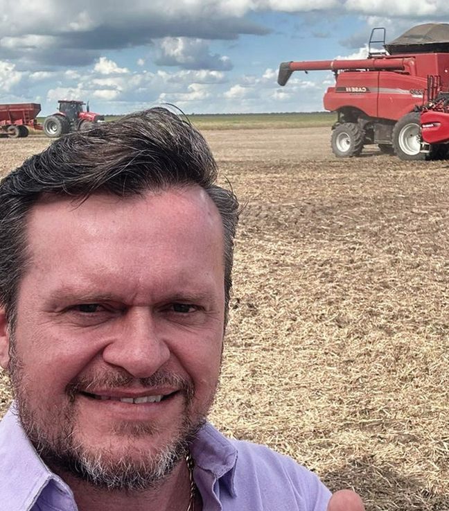 Integrante da equipe AGROJUS em lavoura, com colheitadeira ao fundo